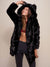 Female model gazing upward and smiling  while holding ear on hood of the fake fur black panther jacket. 