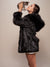 A pretty brown-haired model showing off the side of the Hooded Black Wolf faux fur coat with the hood down, holding a kitten in the air and looking at it lovingly.