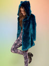 Brown-haired model smiling down with her leg up and bent knee in her Royal Wolf vegan luxe fur coat.