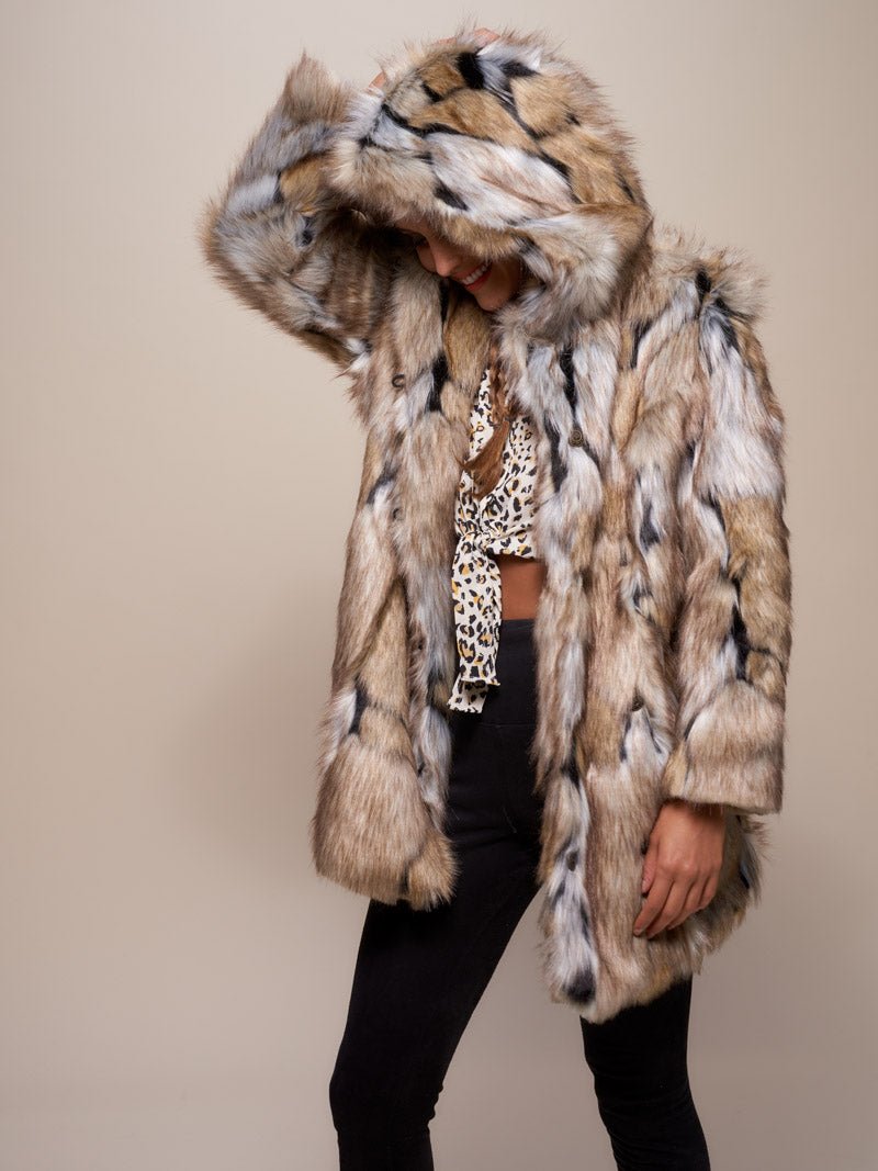 A female model posing with her body slightly angled to the side in a Hooded Wolverine fake fur jacket, with one arm resting on the hood and most of her face covered.