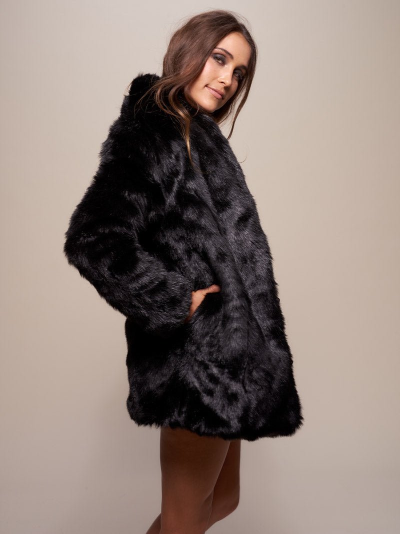 Brown haired female model standing with her body facing to to the right with her hand in the pocket of her panther black fake fur jacket, while her head is turned looking at the camera.