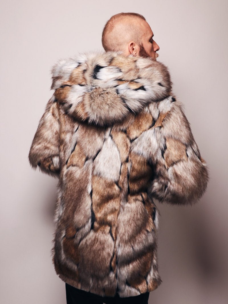 A male model with a buzzed haircut, turned with his back slightly to the side and the hood down, showcasing the vegan Hooded Wolverine fur coat from the back.