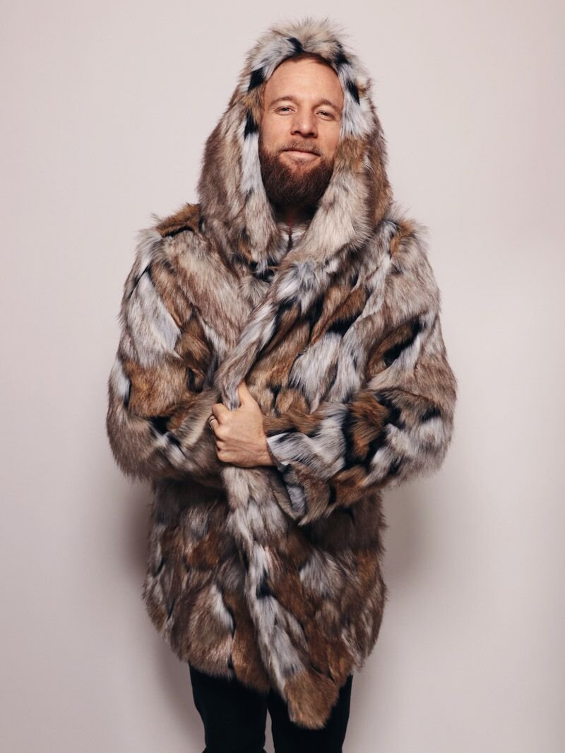 Bearded man wrapped in a Hooded Wolverine faux fur coat, holding it closed at the midsection with the hood up, looking happy and cozy.