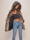 Jean wearing  female model wearing Hooded Grey Wolf fake fur jacket with the hood up while holding it open on one side exposing inner black logo liner.