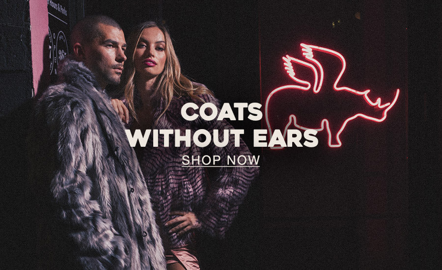 Man a women standing against a wall outdoors at night wearing faux fur coats and a button that says SHOP COATS WITHOUT EARS