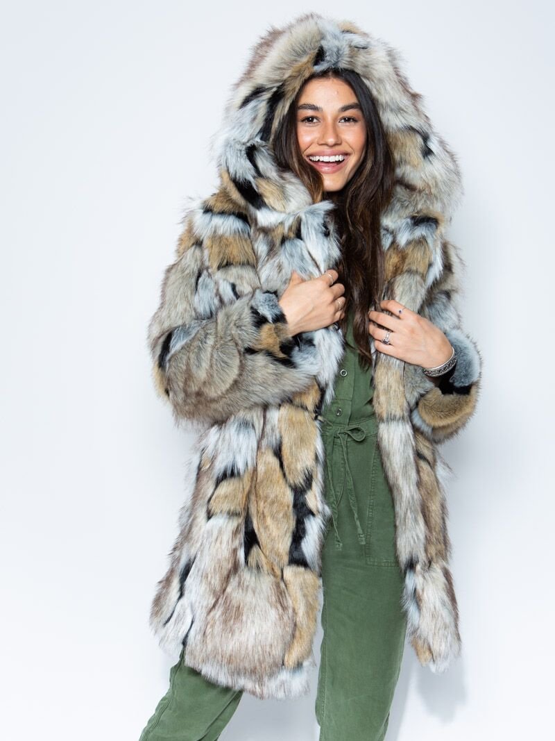 A joyful, brown-haired girl wearing the hood up and holding the lapels of the Hooded Wolverine faux fur coat.