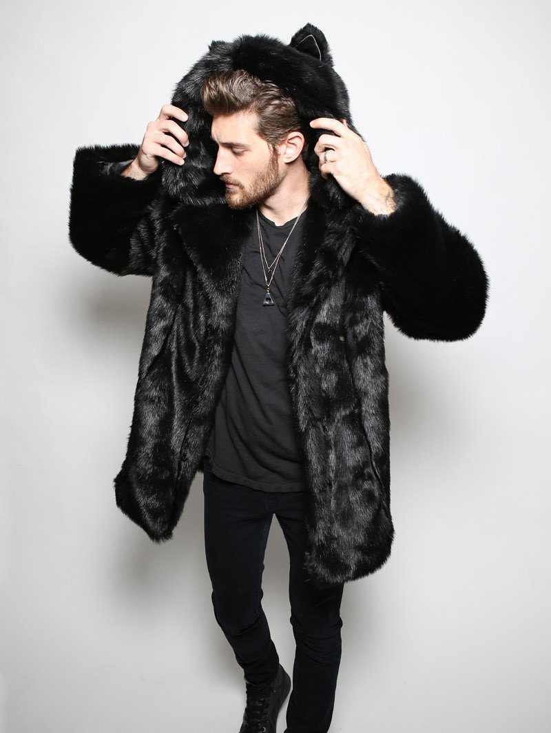 Male model facing slightly to the side with hands raised holding hood and ears of black panther faux fur jacket.