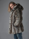 Longish haired blonde male model turned to one side wearing hooded grey wolf fake fur coat with hand in his pocket looking at the camera. 